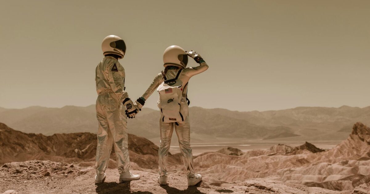 Two astronauts holding hands, exploring rocky Mars-like terrain.