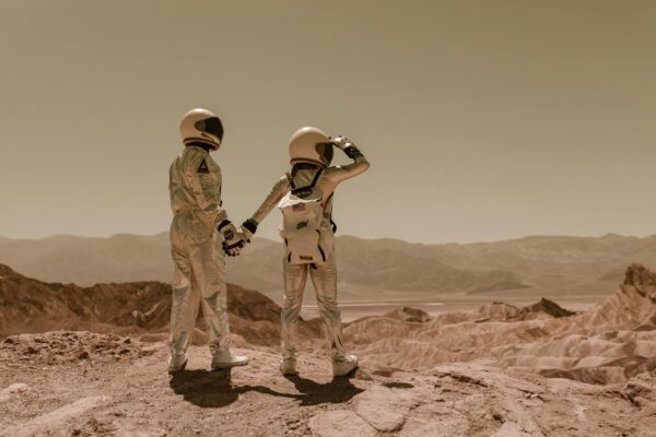 Two astronauts holding hands, exploring rocky Mars-like terrain.