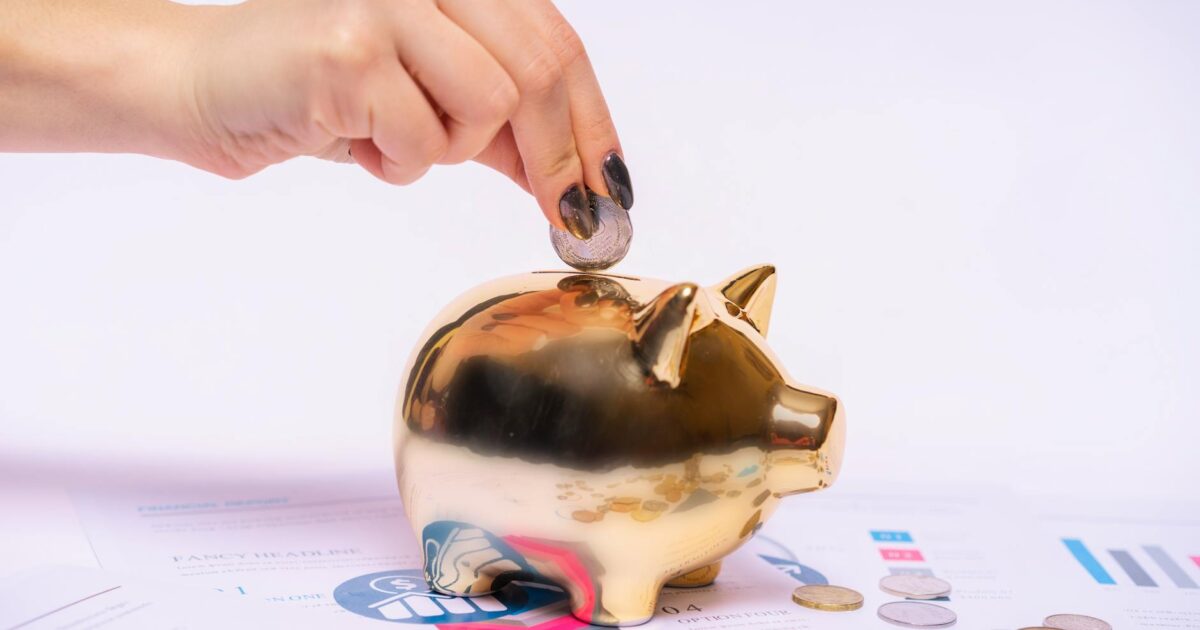 A hand places a coin into a golden piggy bank surrounded by financial documents, symbolizing savings.